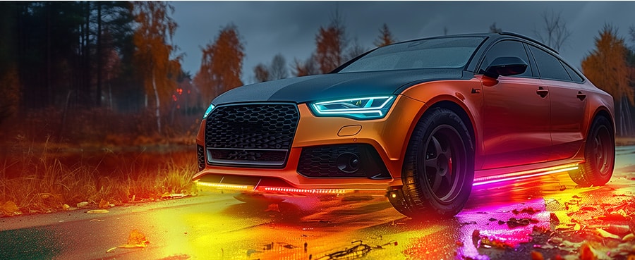 A sportback car with color-changing LED underglow on fall road, showcasing vibrant lighting against autumn foliage.